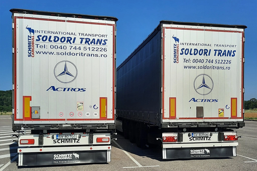 Semi-remorcile Schmitz din flota de transport international inscriptionate cu numele si datle de contact ale companiei